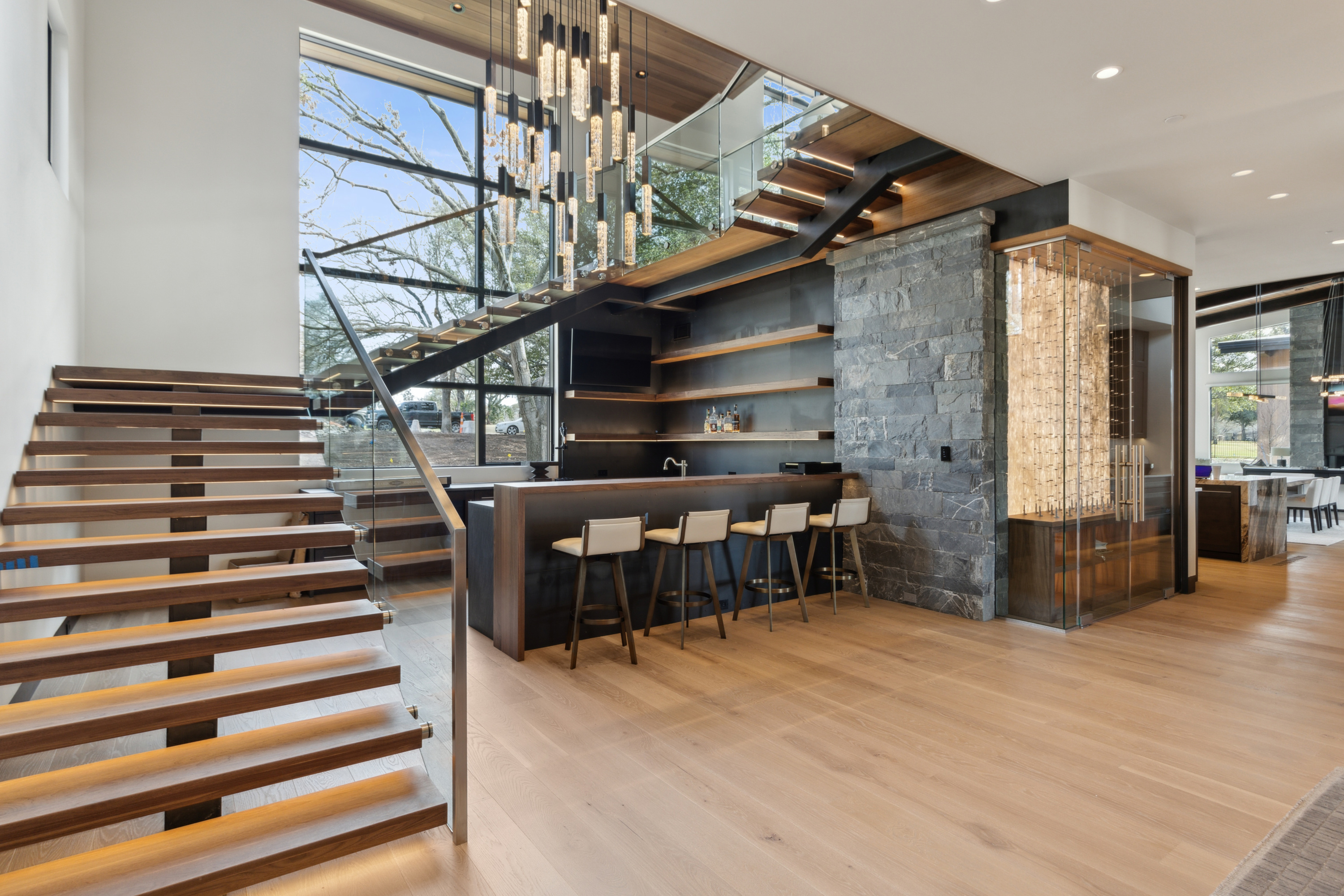 Luxury custom home interior with floating staircase, custom bar, and floor-to-ceiling windows