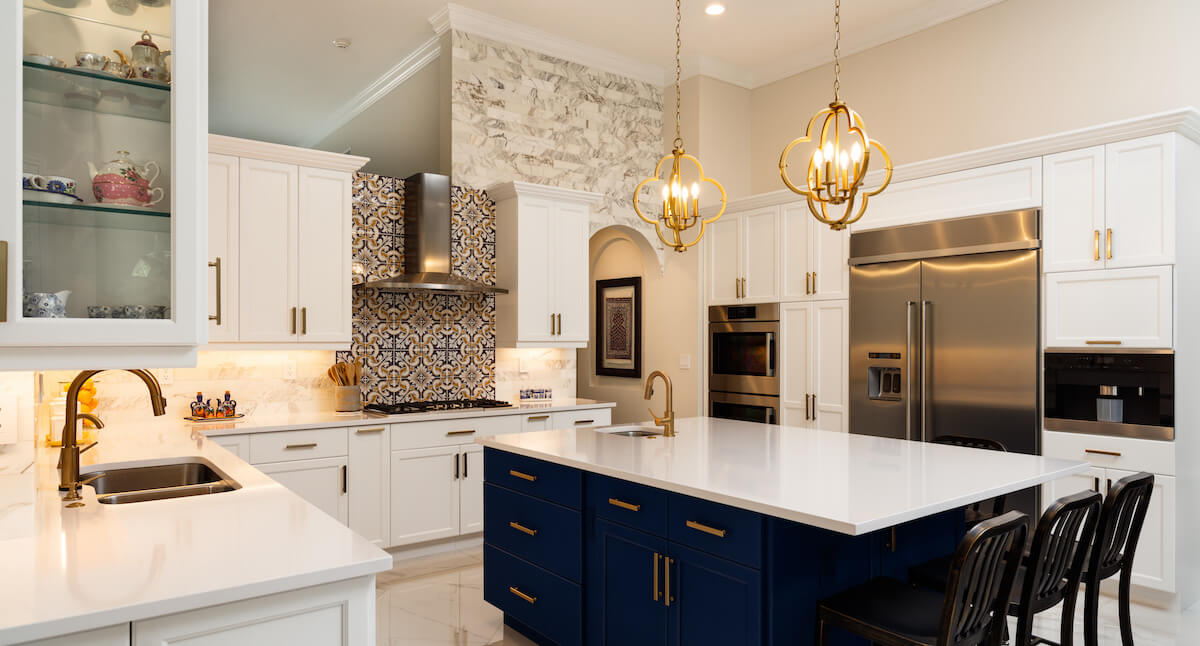 Elegant kitchen with navy island, marble accents, and quatrefoil chandeliers