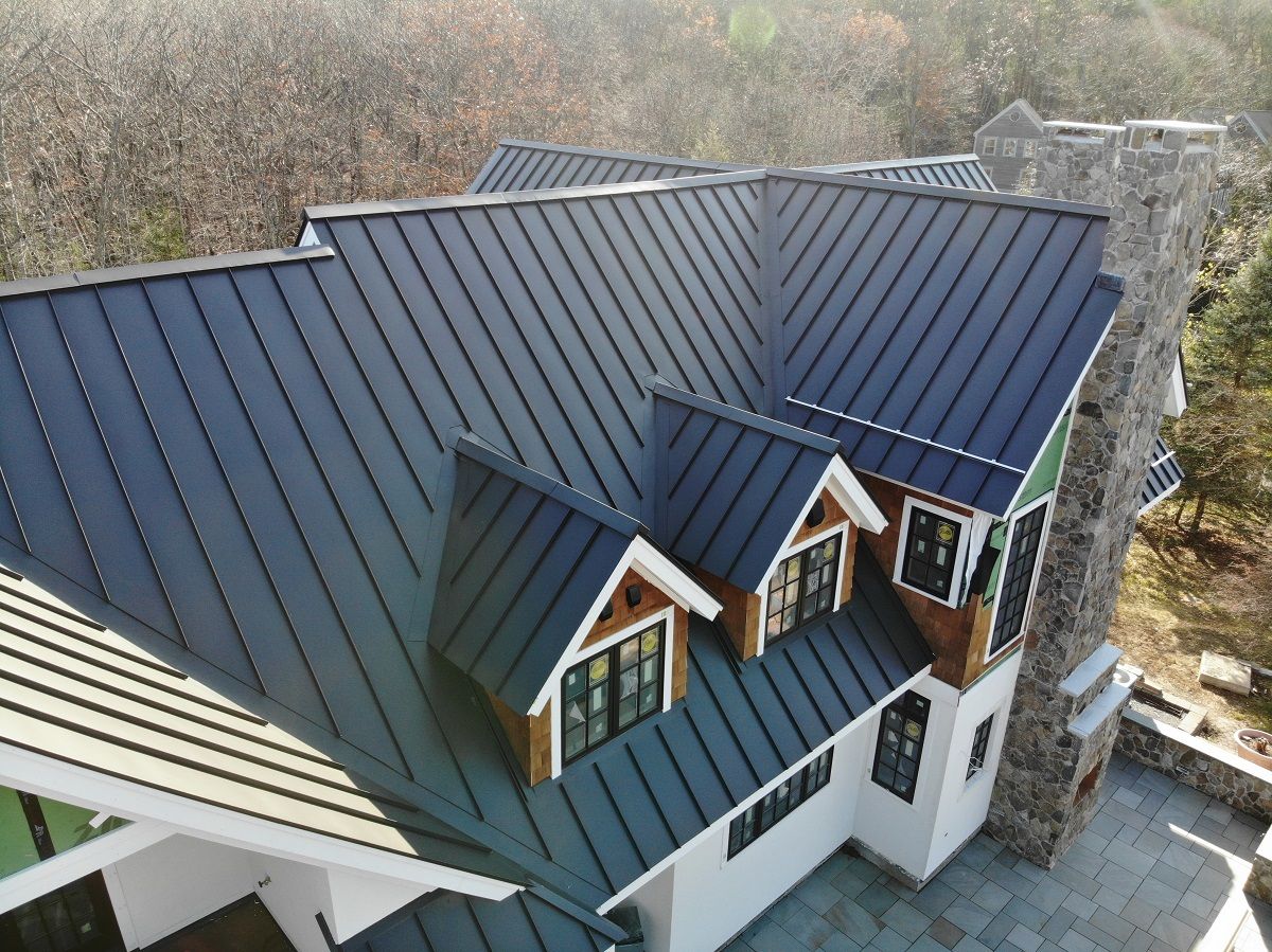 Multi-gable standing seam metal roof with dormer windows and stone chimney