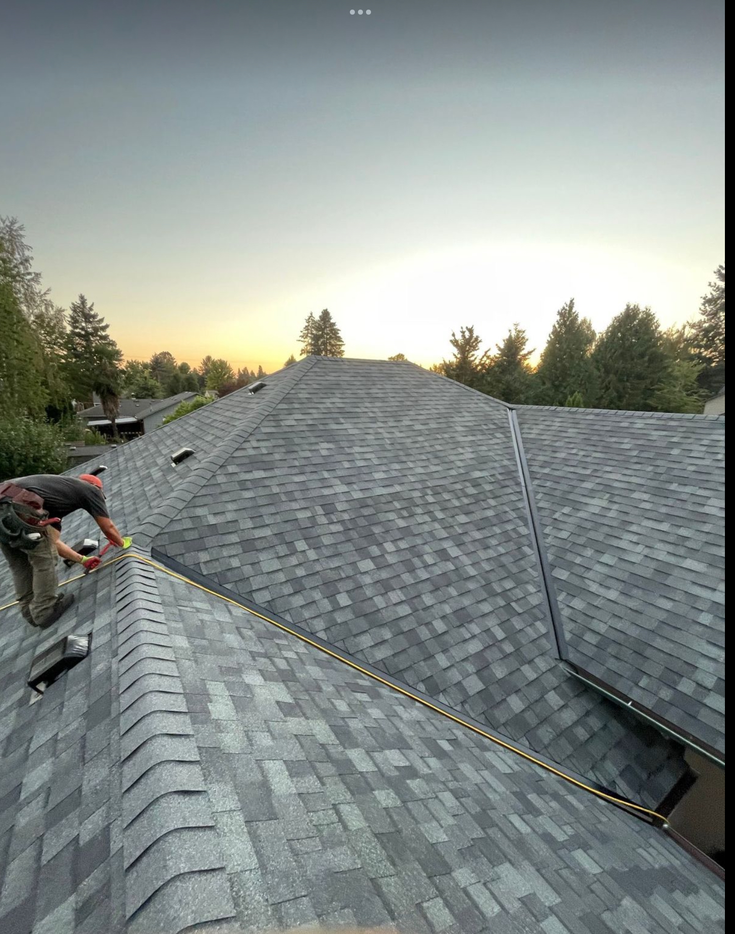 Shingle roof installation at sunset with crew on site